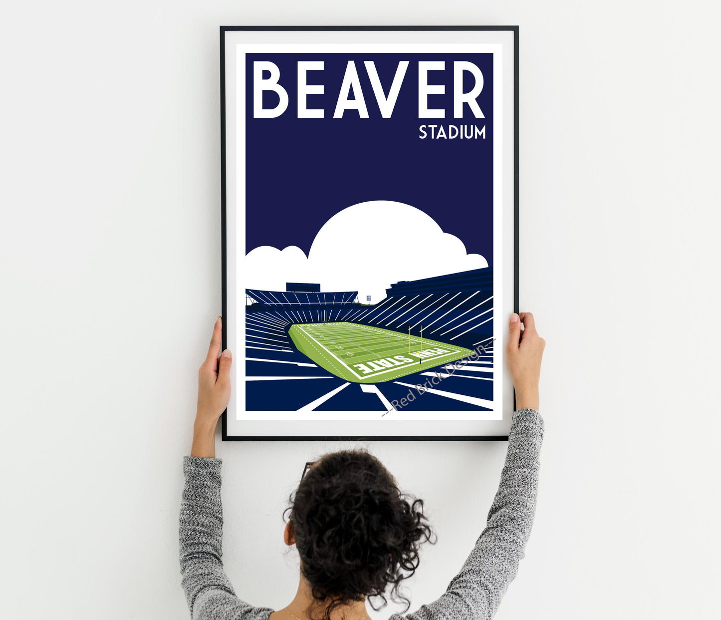 a woman holding up a framed poster of a stadium