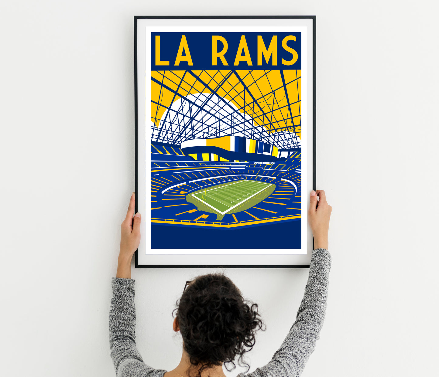 a woman holding up a framed poster of a stadium