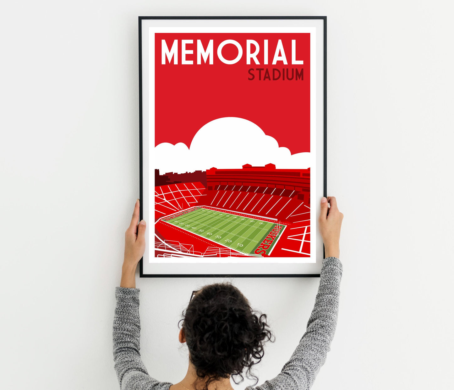 a woman holding up a framed poster of a stadium