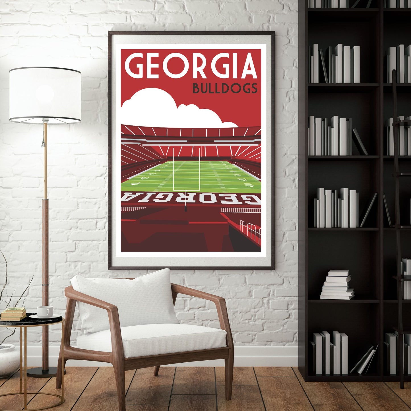a framed poster of a football stadium with the text "GEORGIA BULLDOGS" on it, hanging on a wall in a room with a white chair and a bookshelf.