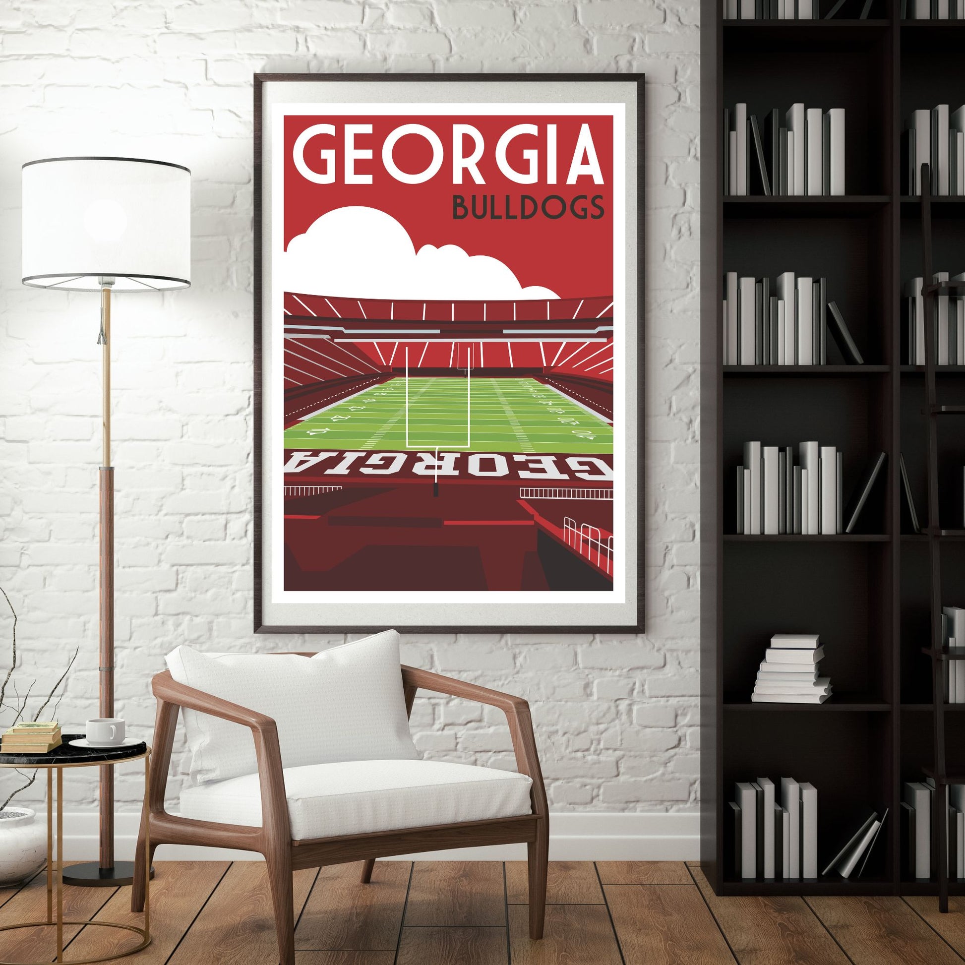 a framed poster of a football stadium with the text "GEORGIA BULLDOGS" on it, hanging on a wall in a room with a white chair and a bookshelf.