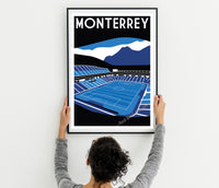 A person is holding up a framed poster of a soccer stadium, which features a mountain landscape in the background.