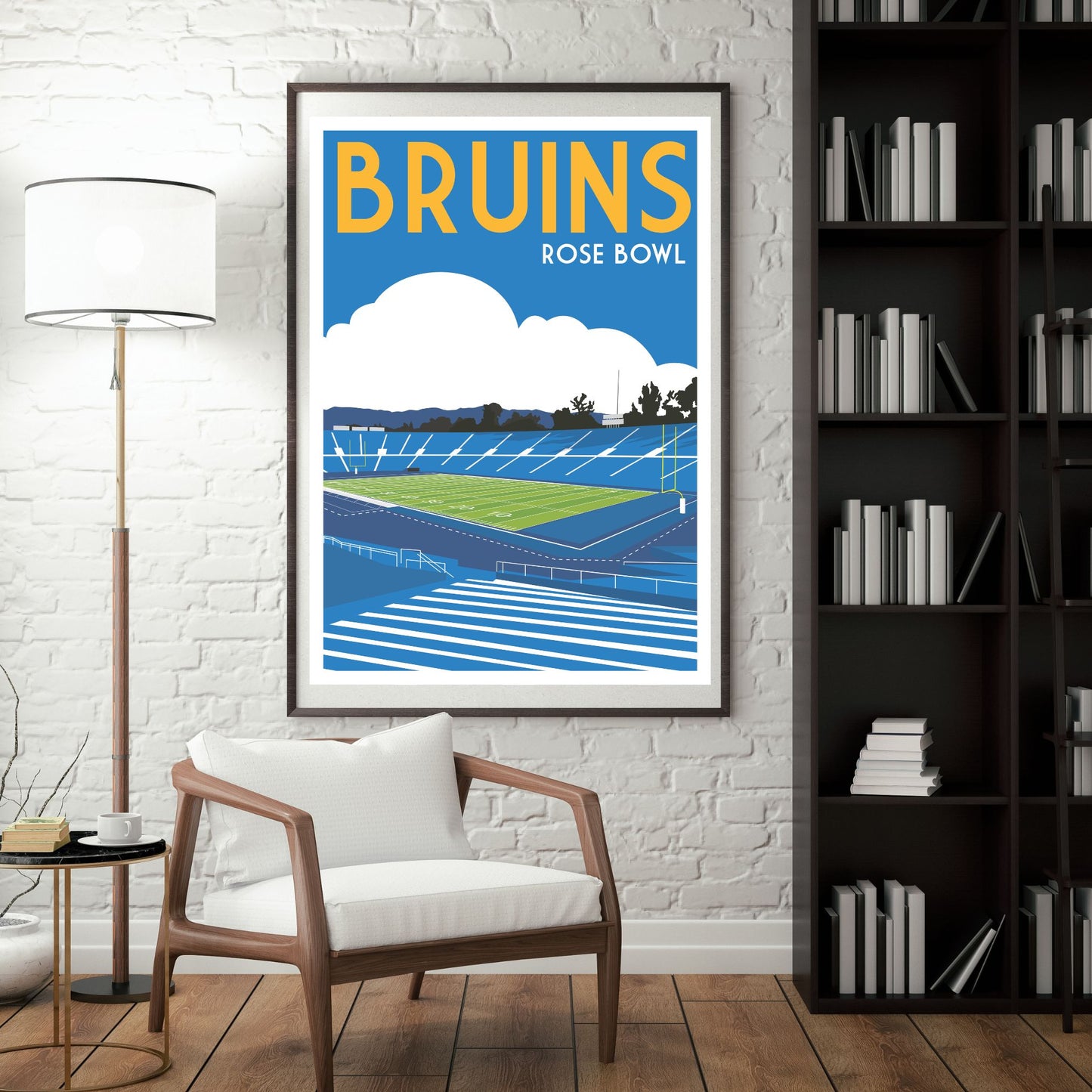 a framed poster of a sports stadium, specifically the Bruins Rose Bowl, hanging on a wall in a room with a bookshelf and a chair.