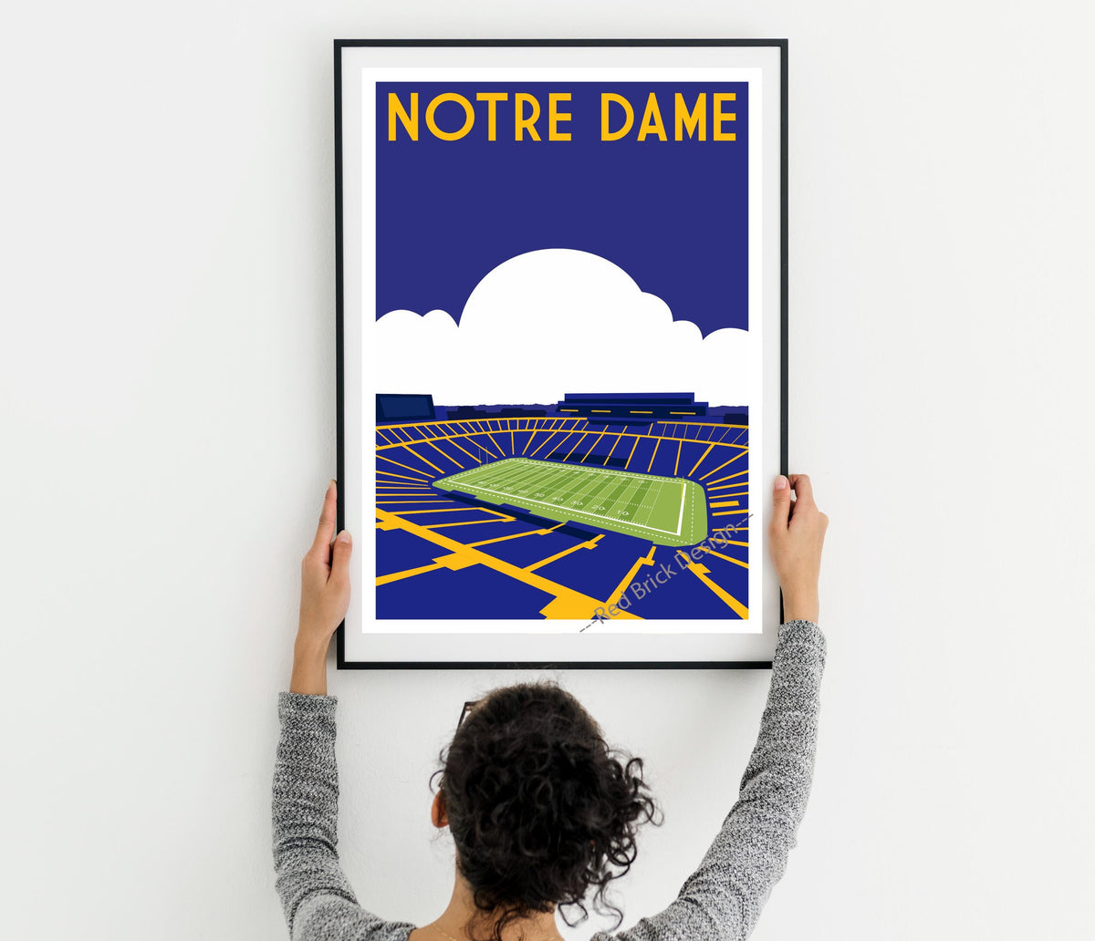 a woman holding up a framed poster of a stadium