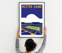 a woman holding up a framed poster of a stadium