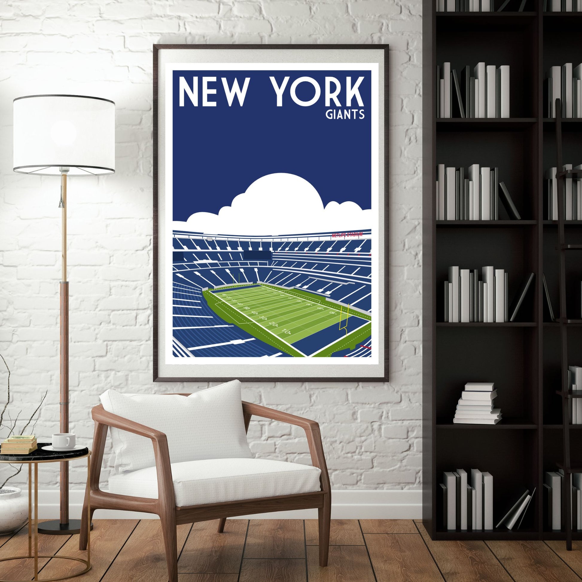 a framed poster of a football stadium with the text "NEW YORK GIANTS" on it, hanging on a wall in a room with a bookshelf and a chair.
