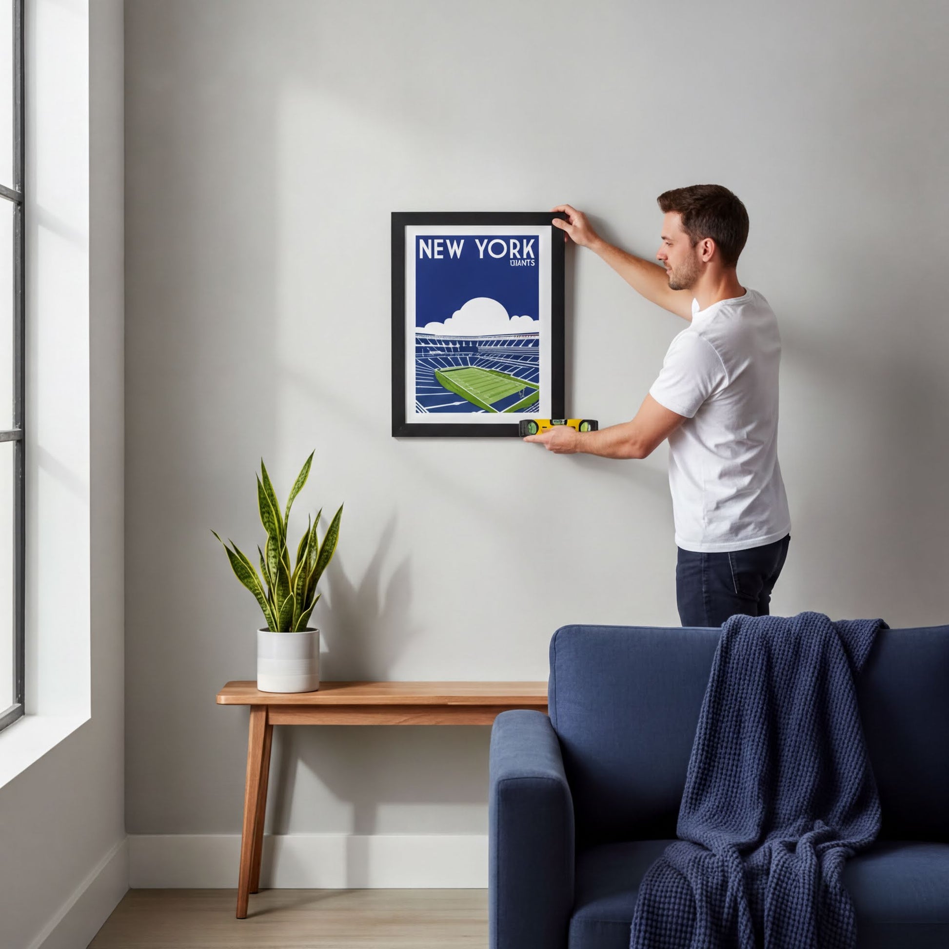 A man is hanging a framed poster of a stadium on a wall in a living room.