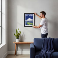 A man is hanging a framed poster of a stadium on a wall in a living room.