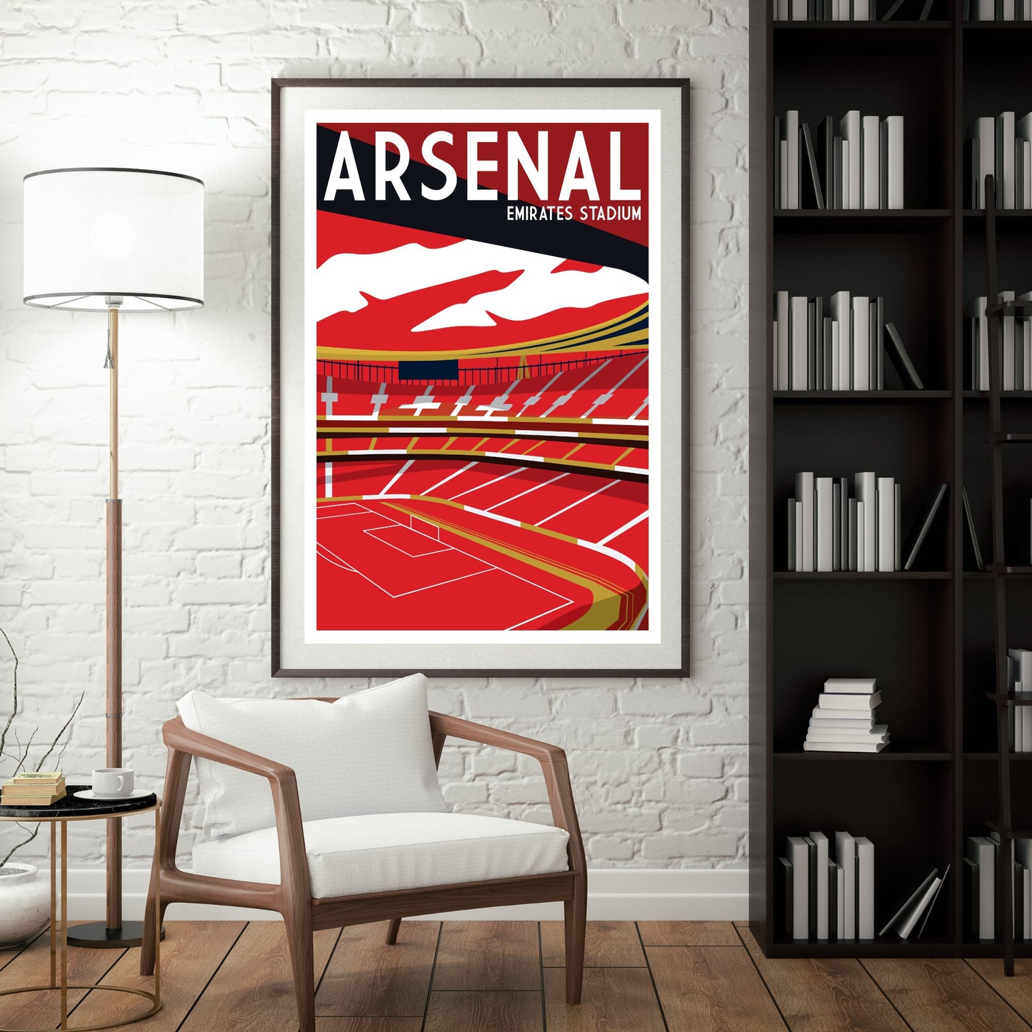 a framed poster of Arsenal Emirates Stadium hanging on a wall, with a white chair in the foreground and a bookshelf filled with books to the right.