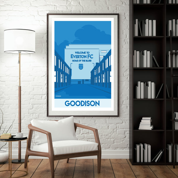 a framed poster of a building with a sign that says "Welcome to Everton FC Home of the Blues" and the word "Goodison" below it. The poster is hanging on a wall next to a bookshelf filled with books.