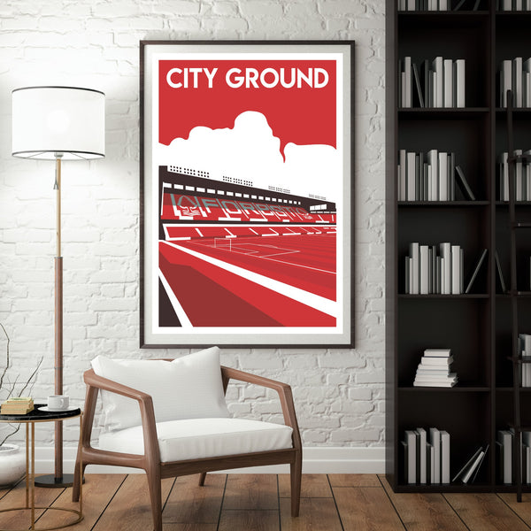 a framed poster of a stadium with a red and white color scheme, hanging on a white brick wall. In front of the poster, there is a white chair, and a bookshelf filled with books can be seen in the background.