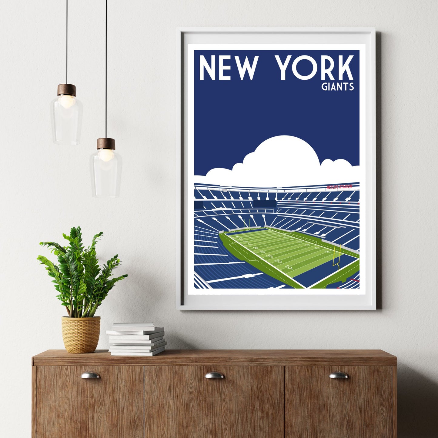 a framed poster of a football stadium with the text "NEW YORK GIANTS" on it, hanging on a wall above a wooden dresser.