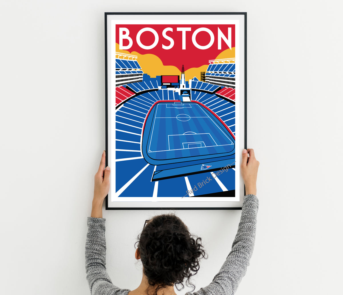 A person is holding up a framed poster of a soccer stadium in Boston.