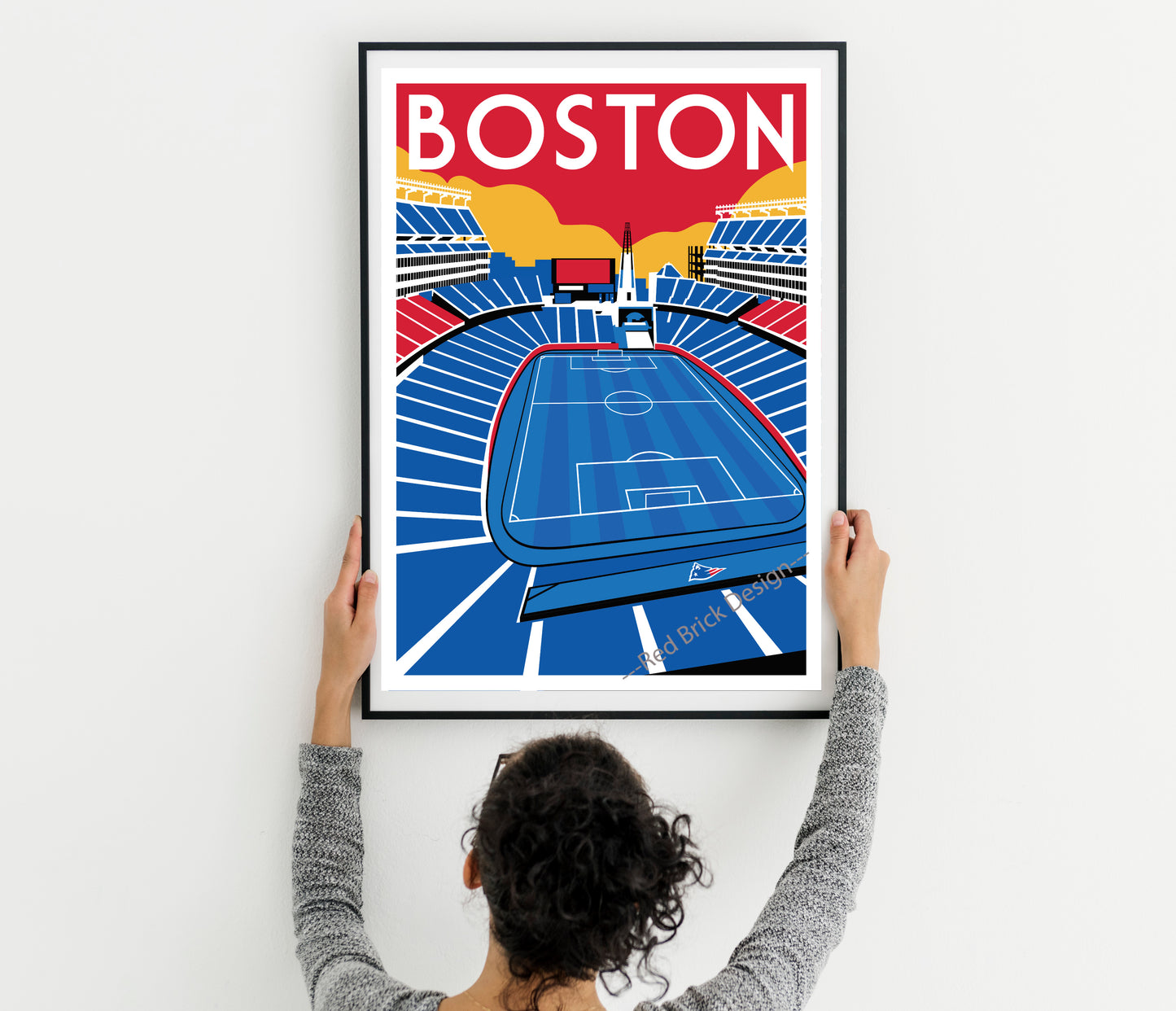 A person is holding up a framed poster of a soccer stadium in Boston.
