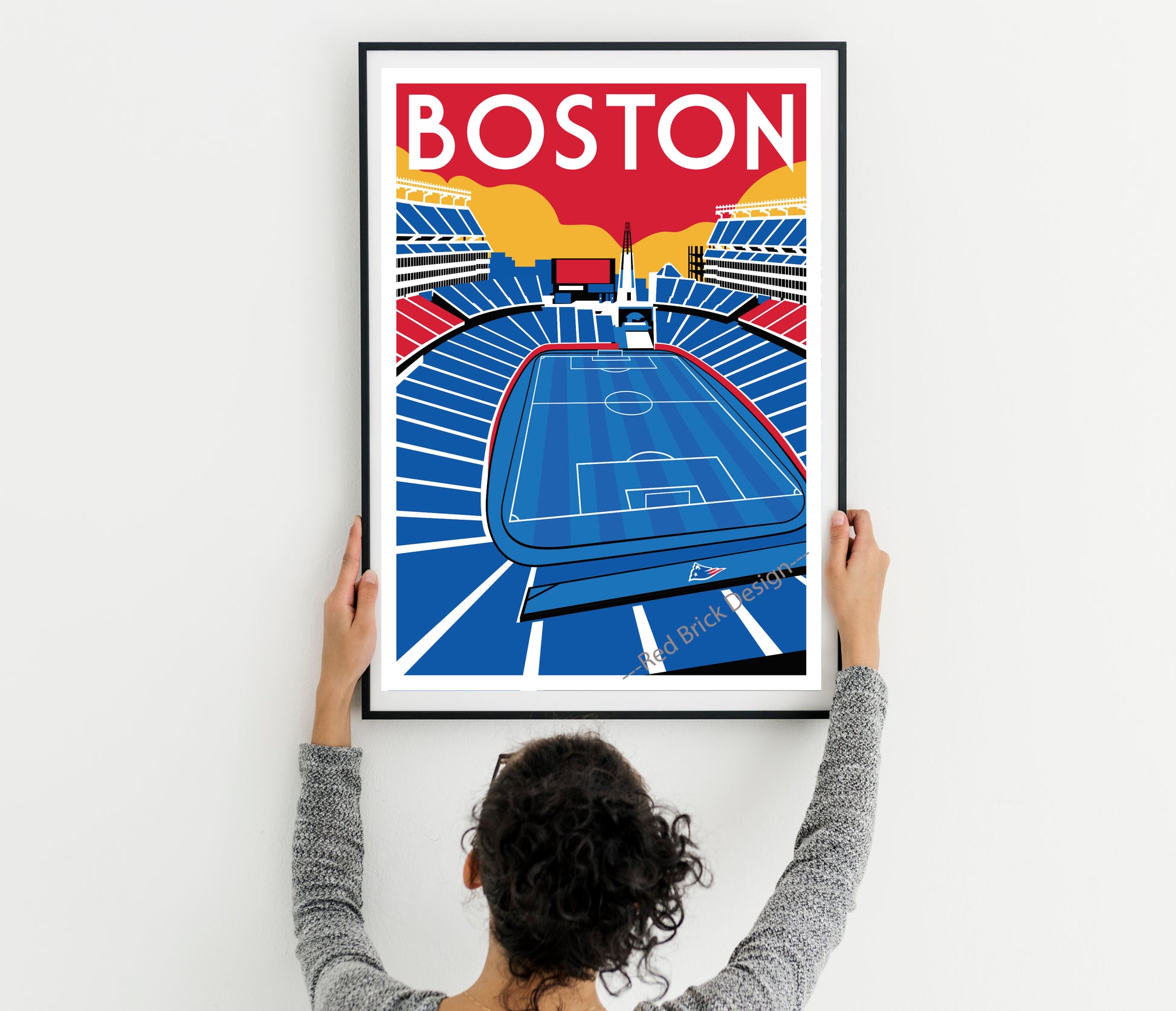 A person is holding up a framed poster of a soccer stadium in Boston.