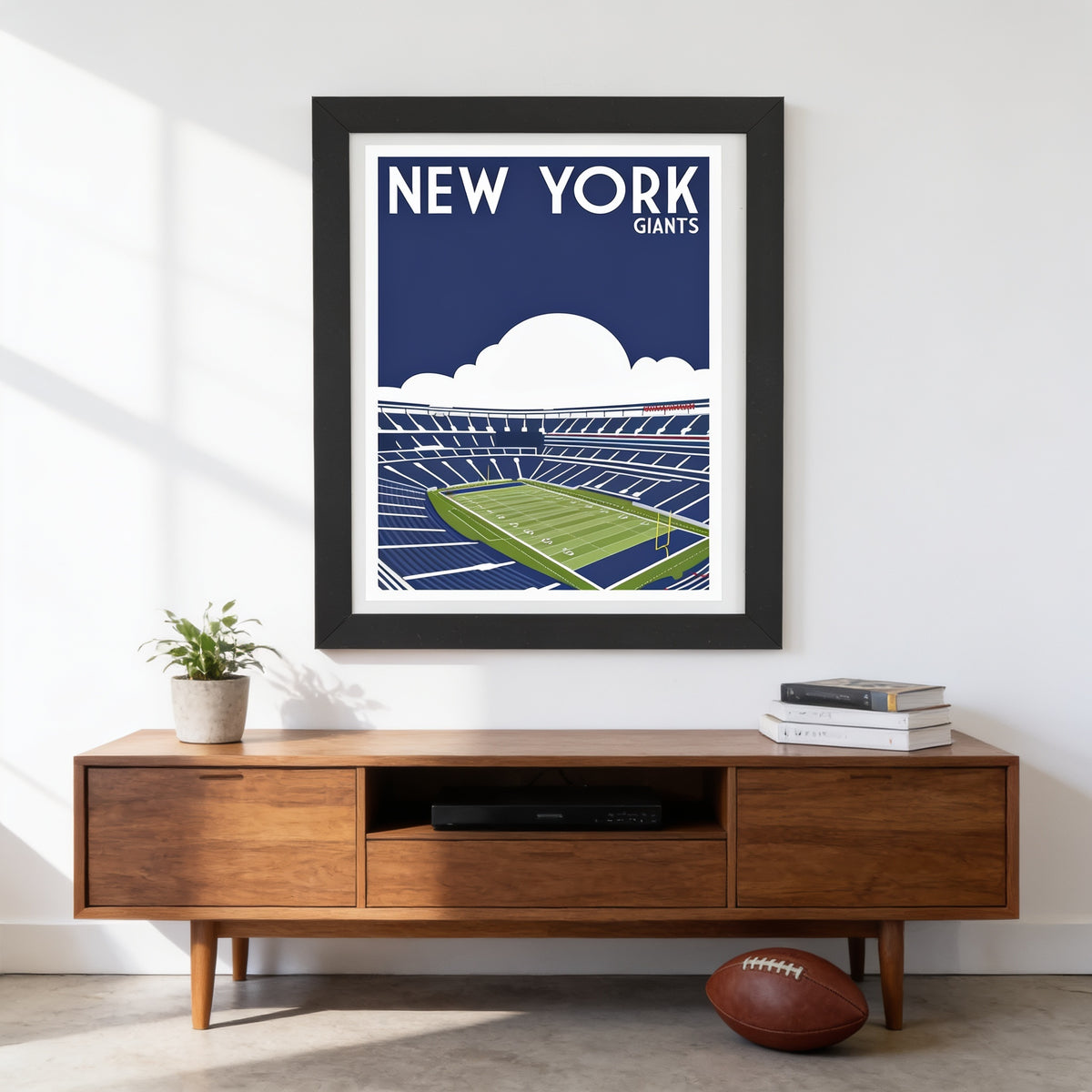 a framed poster of a football stadium with the text "NEW YORK GIANTS" on it, hanging on a wall above a wooden entertainment center with a television and a football.