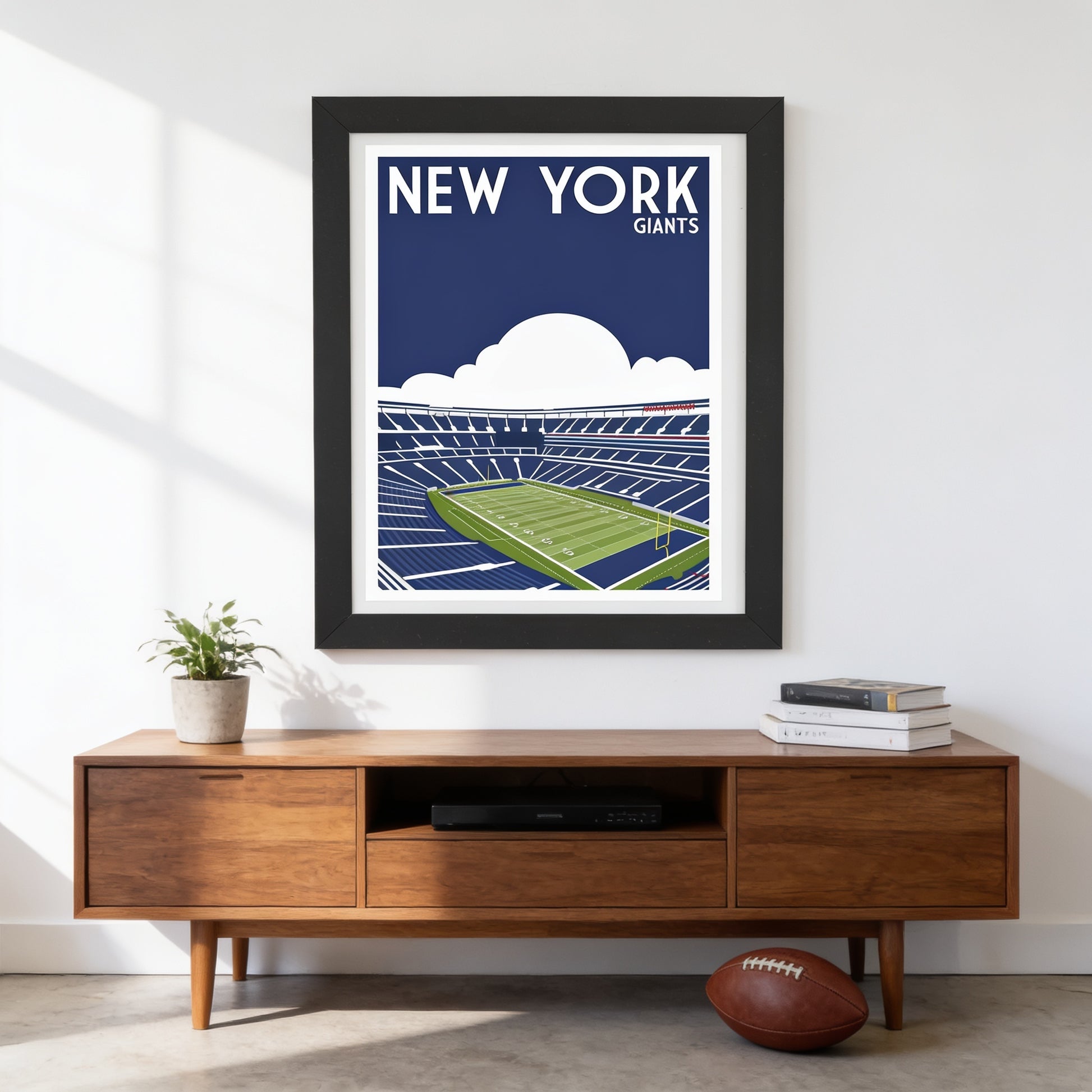 a framed poster of a football stadium with the text "NEW YORK GIANTS" on it, hanging on a wall above a wooden entertainment center with a television and a football.