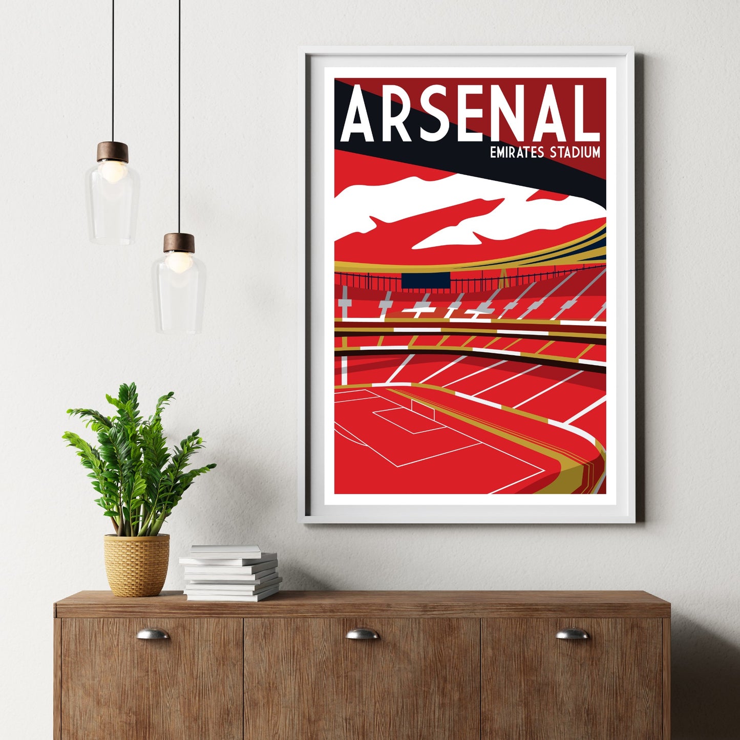 a framed poster of Arsenal Emirates Stadium hanging on a wall, with a potted plant and a wooden cabinet below it.