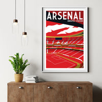 a framed poster of Arsenal Emirates Stadium hanging on a wall, with a potted plant and a wooden cabinet below it.