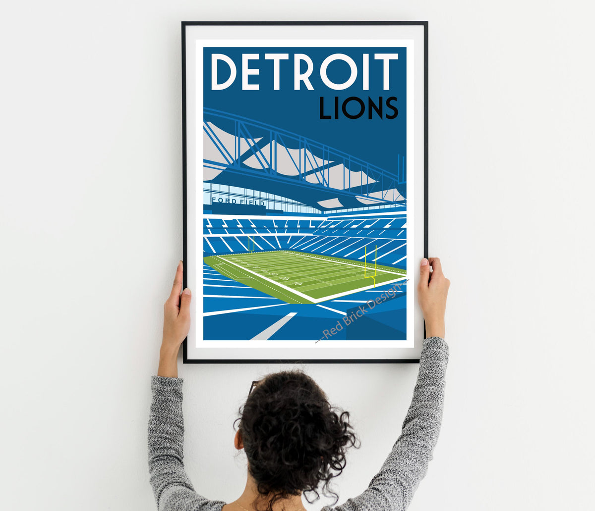 a woman holding up a framed poster of a stadium