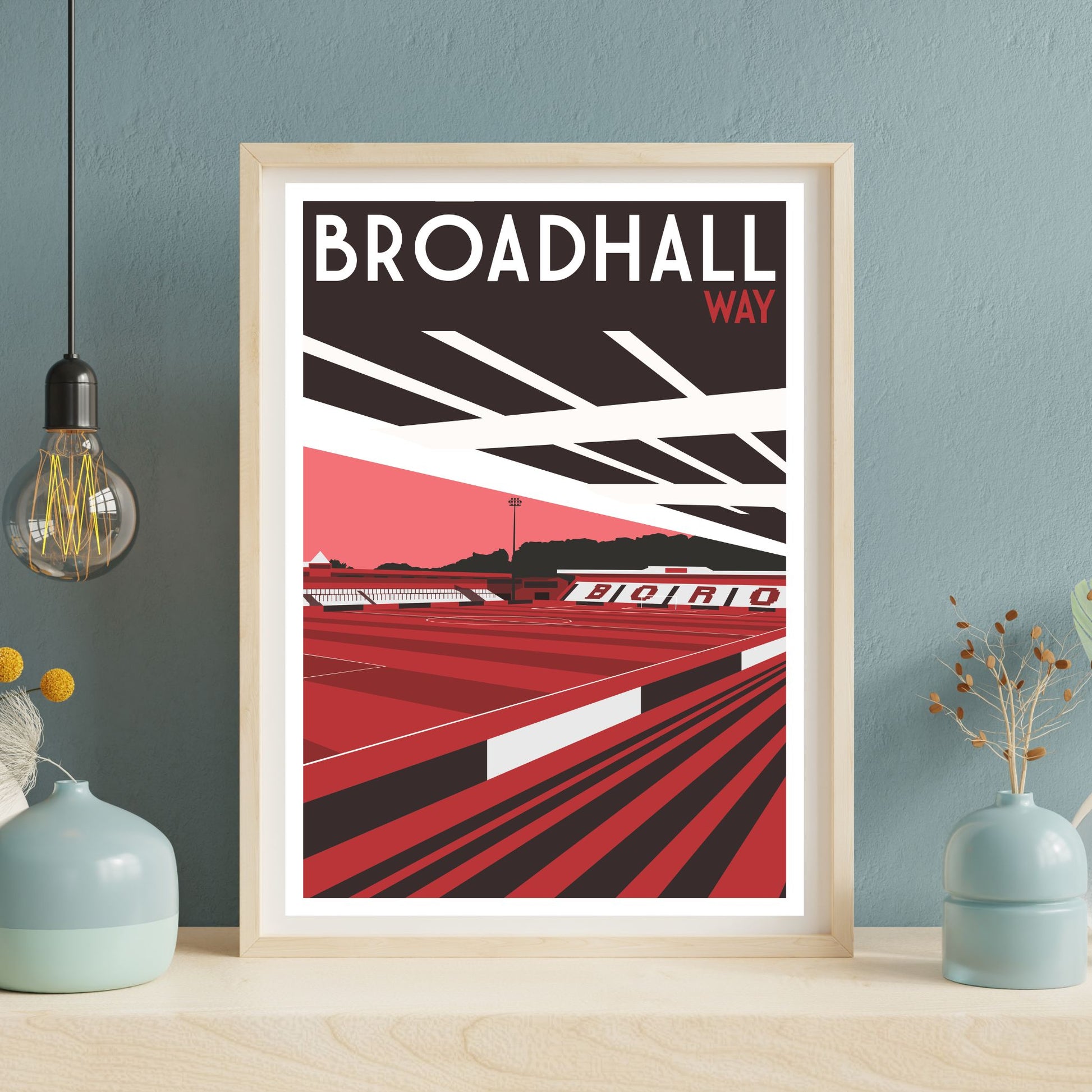 a framed poster of a sports stadium, specifically Broadhall Way, with a red and black color scheme.