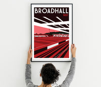 A person is holding up a framed poster of Broad Hall Way, which features a red and black design with a stadium and track.