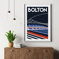 a framed poster of a stadium with a bridge in the background, hanging on a wall above a wooden dresser with a stack of books and a potted plant.