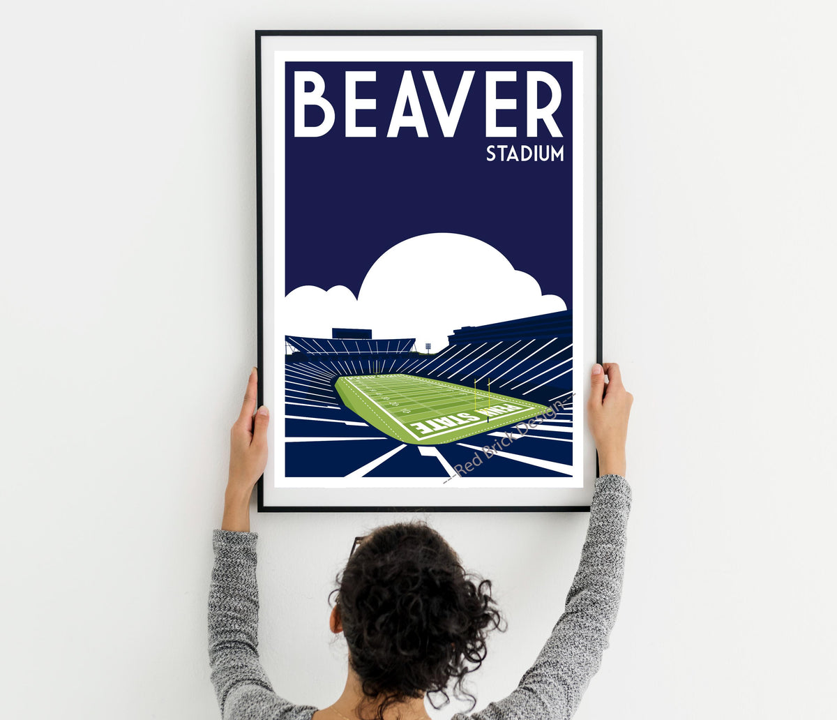 a woman holding up a framed poster of a stadium