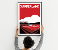 A person is holding up a framed poster of a stadium with the word "Sunderland" written on it.