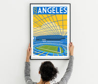 A person is hanging a framed poster of a stadium on a wall.