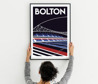 A person is hanging a framed poster of a stadium on a wall.