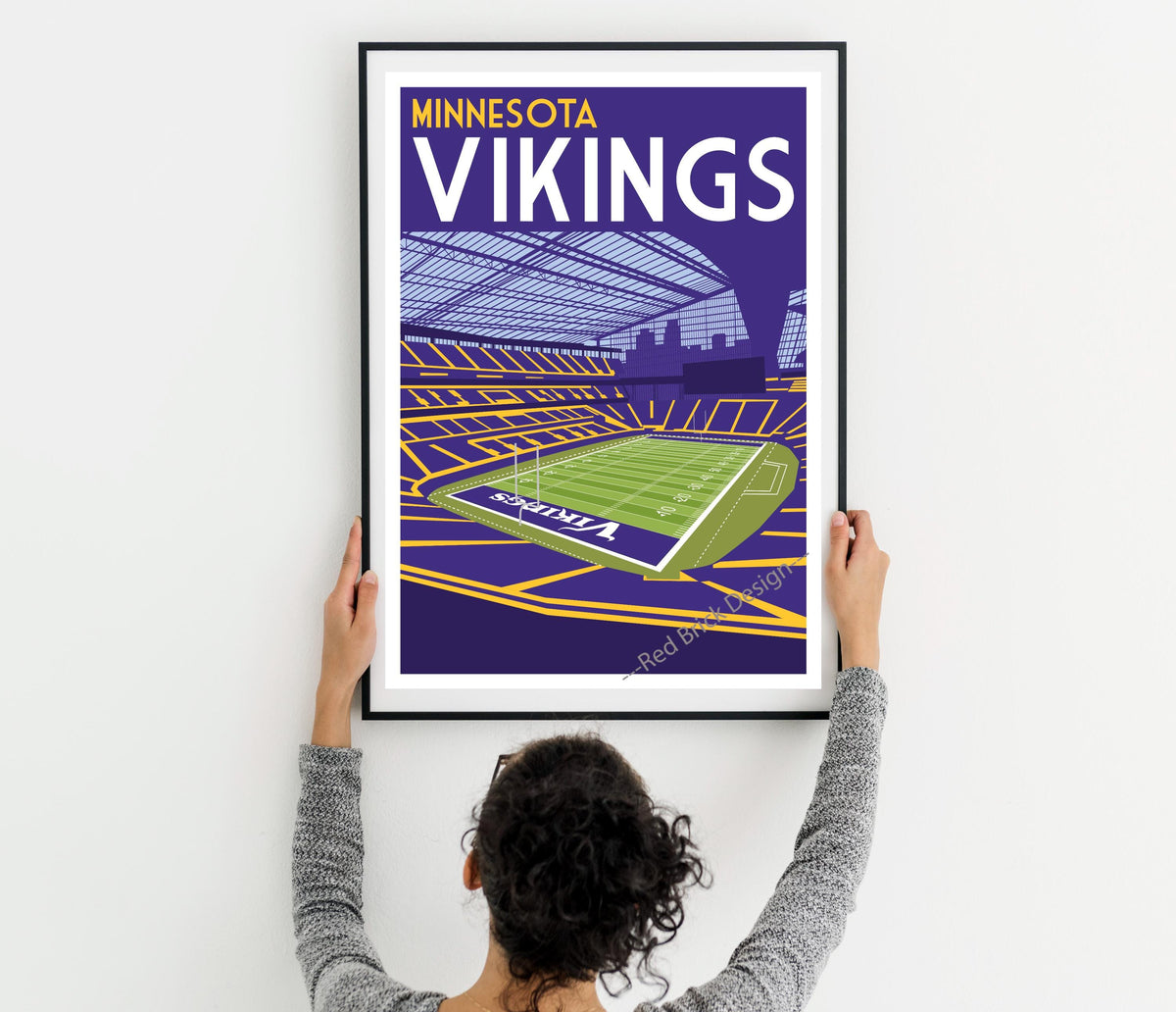 a woman holding up a framed poster of minnesota vikings