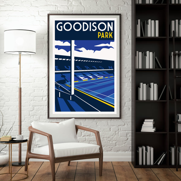 a framed poster of Goodison Park, a sports stadium, hanging on a wall in a room with a white chair and a bookshelf.