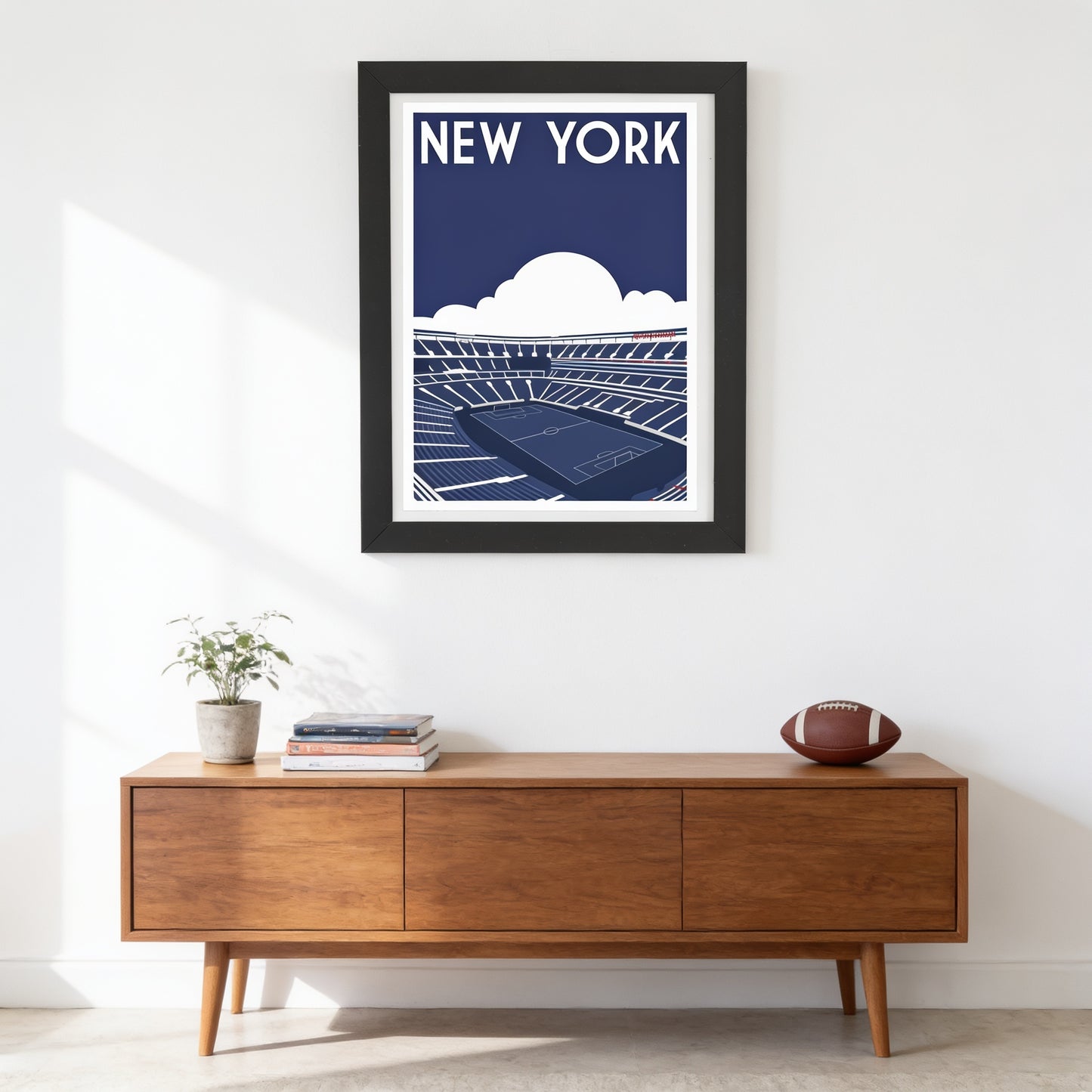 a framed poster of a stadium with a tennis court, hanging on a wall above a wooden cabinet with a football on top.