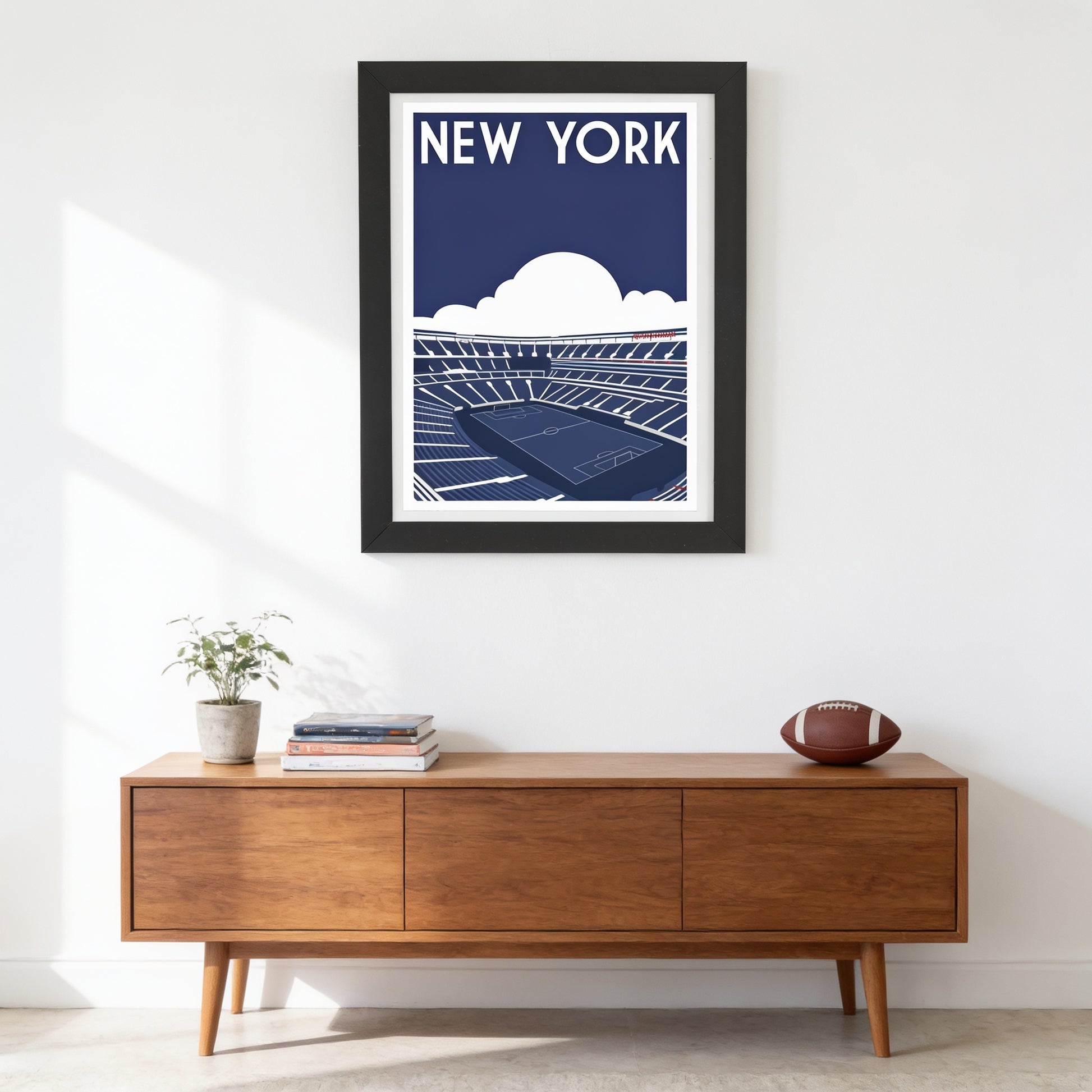 a framed poster of a stadium with a tennis court, hanging on a wall above a wooden cabinet with a football on top.