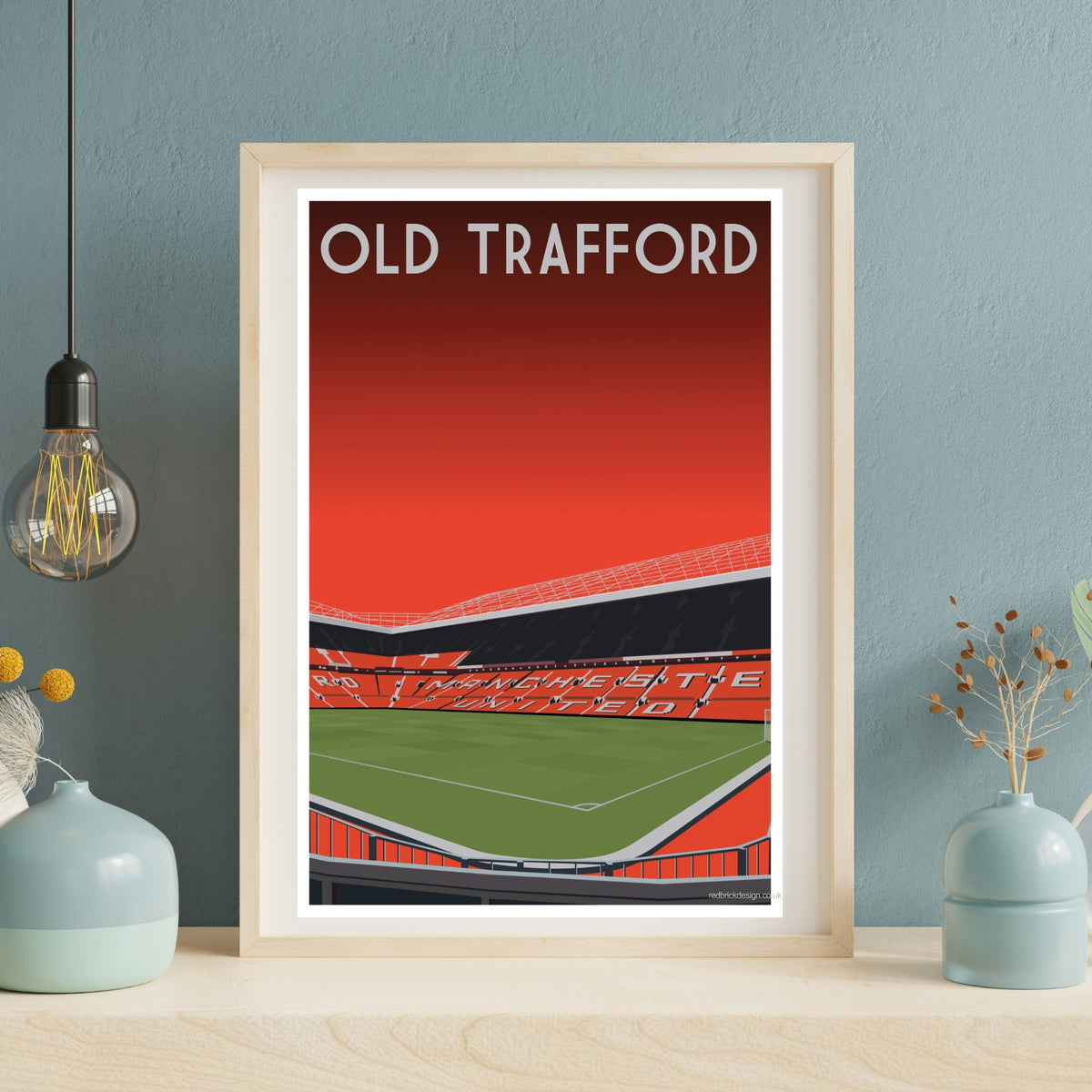 a framed poster of a football stadium with a red and green color scheme, displaying the text "OLD TRAFFORD" prominently.
