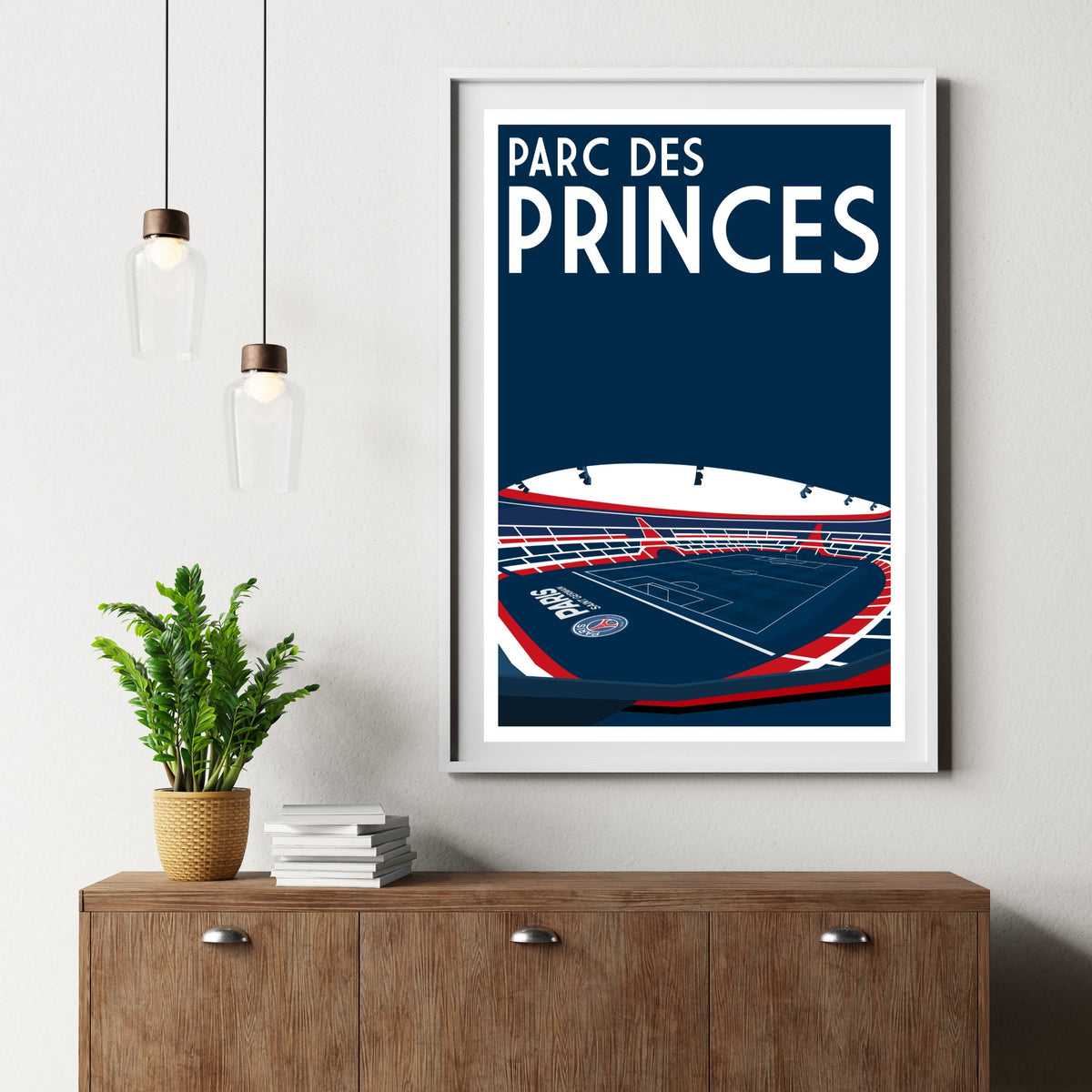 a framed poster of a stadium with the text "PARC DES PRINCES" on it, hanging on a wall above a wooden dresser.