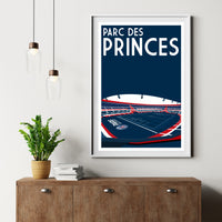 a framed poster of a stadium with the text "PARC DES PRINCES" on it, hanging on a wall above a wooden dresser.