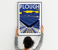 A person is hanging a framed poster of a stadium on a wall.