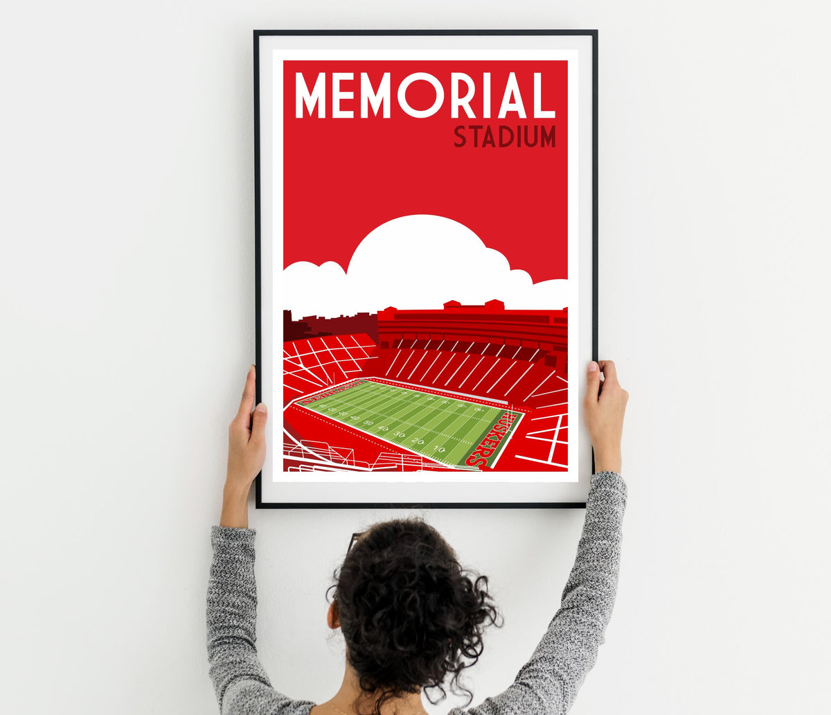 a woman holding up a framed poster of a stadium