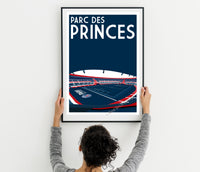A person is hanging a framed poster of a stadium with the text "PARC DES PRINCES" on it.