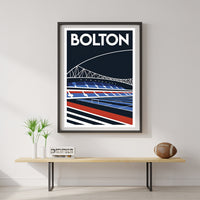 a framed poster of a stadium with a football field, hanging on a wall above a wooden table with a plant and a football.