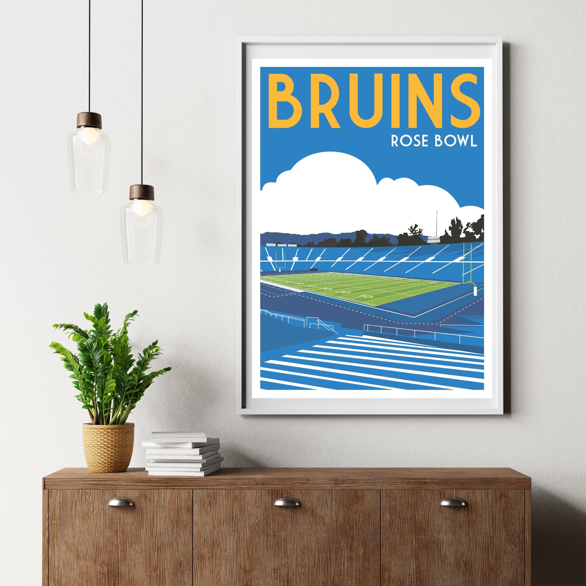 a framed poster of a sports stadium, specifically the Bruins Rose Bowl, hanging on a wall above a wooden cabinet.