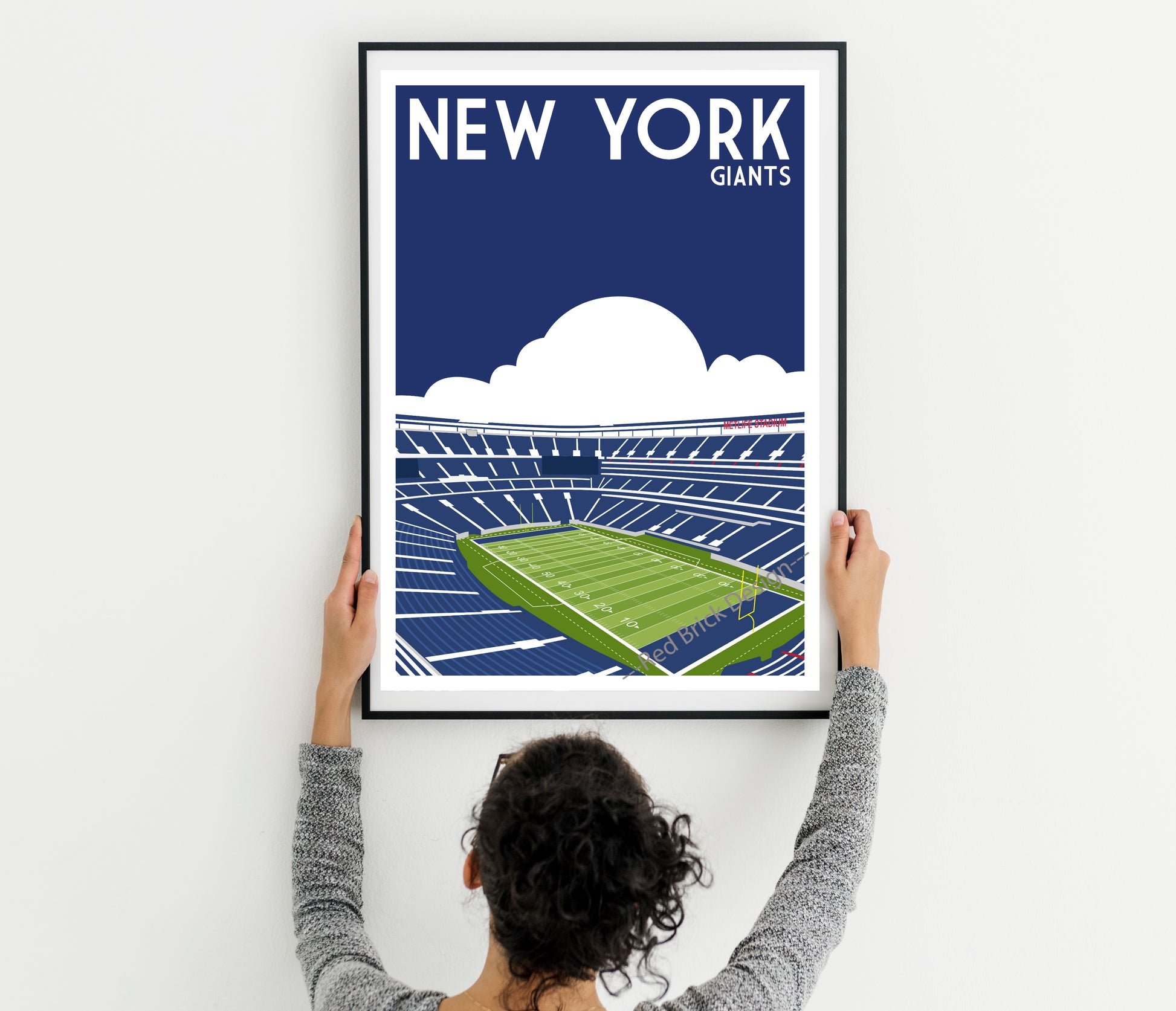 A person is holding up a framed poster of a football stadium, with the words "NEW YORK GIANTS" written on it.