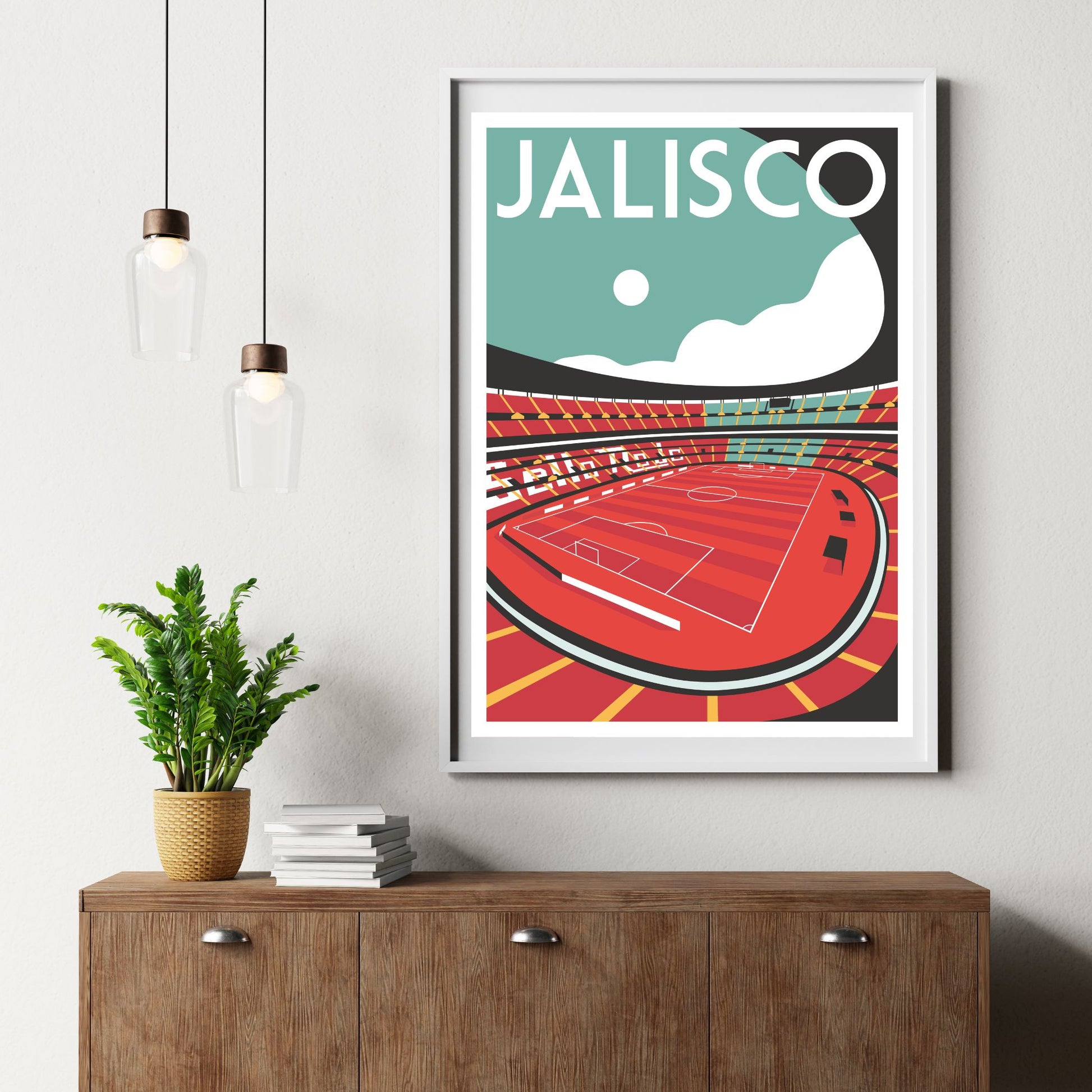 a framed poster of a soccer stadium, with a potted plant and a stack of books on a wooden dresser below it.