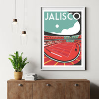 a framed poster of a soccer stadium, with a potted plant and a stack of books on a wooden dresser below it.