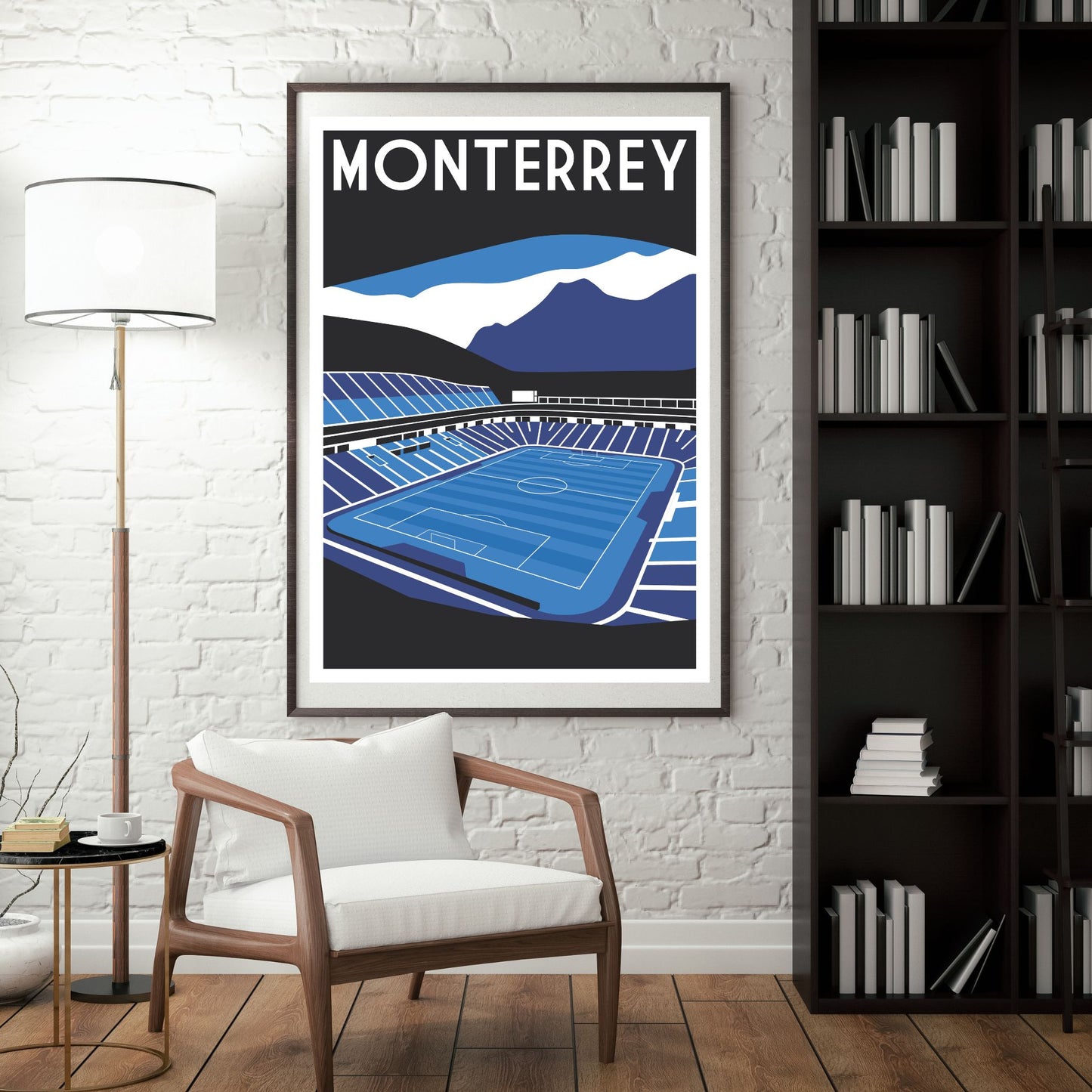 a framed poster of a soccer stadium, with mountains in the background, hanging on a wall next to a bookshelf.